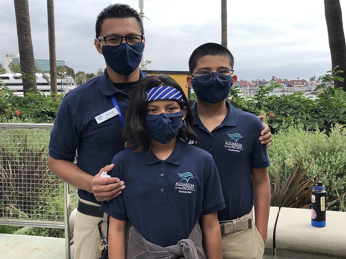 Family volunteers (a father and two children) pose for a photo on Harbor Terrace.